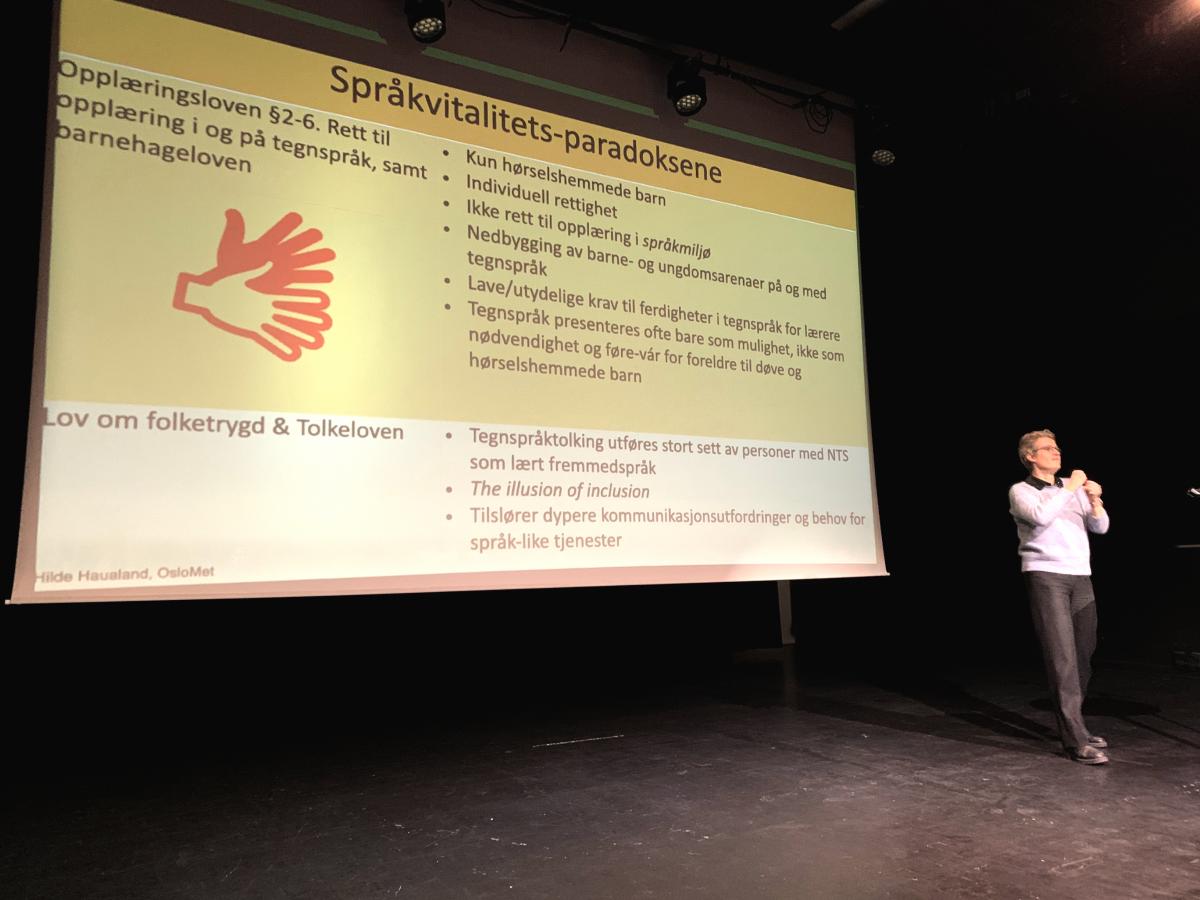 Janne Langaas, teatersjef fra Teater Manu holder foredrag. Damen som står ved siden av Janne er tegnspråktolk.